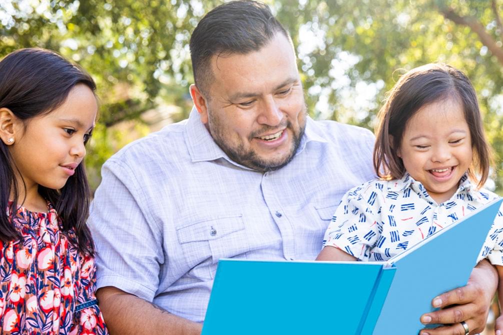 A man and a child smiling while reading a book
